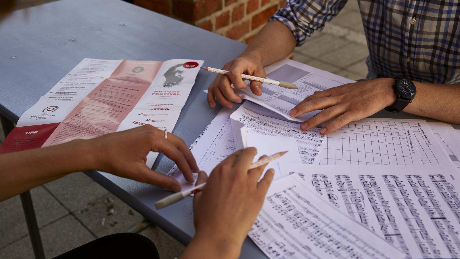 Blick auf vier Hände, die auf einem Tisch unterschiedliche Musiknoten sortieren
