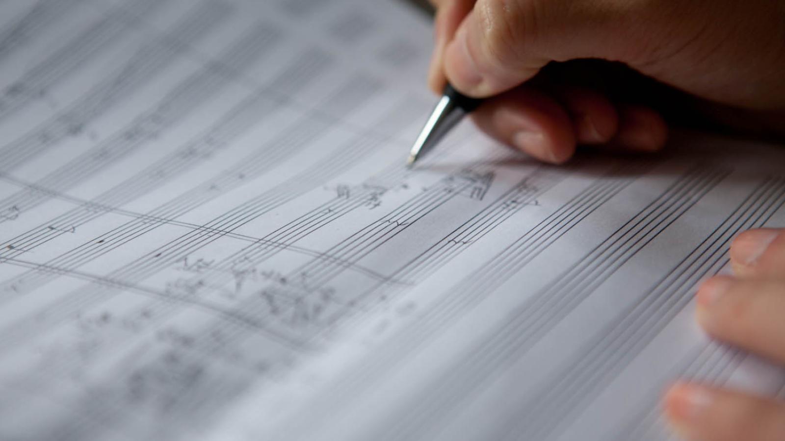 Blick auf eine Hand, die Noten auf Notenpapier schreibt.