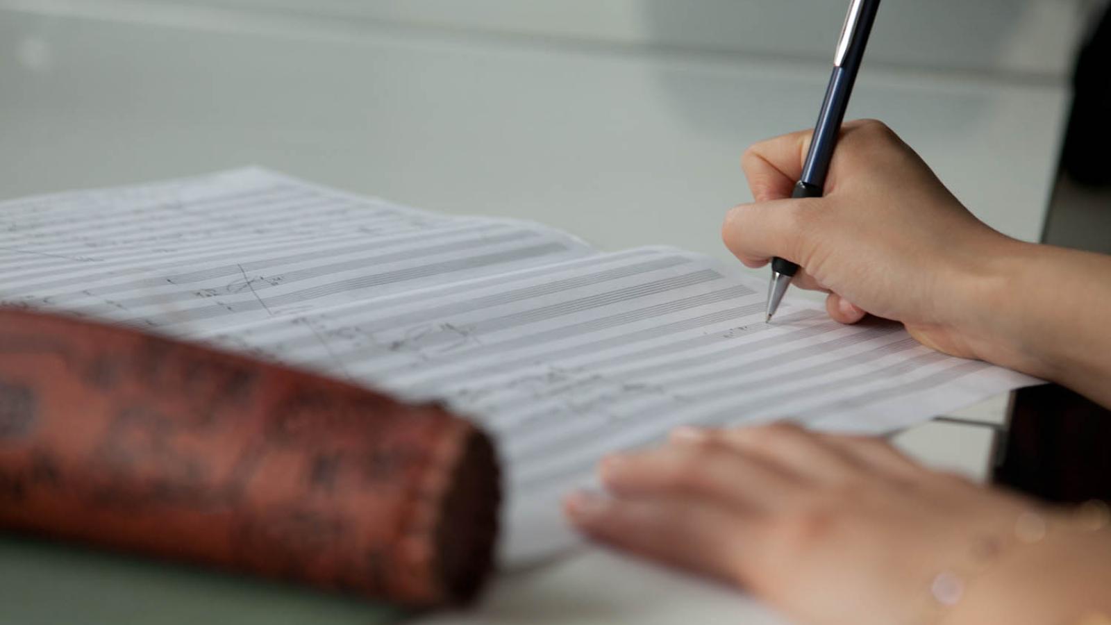 Eine Studentin notiert Musik auf ein Blatt Notenpapier