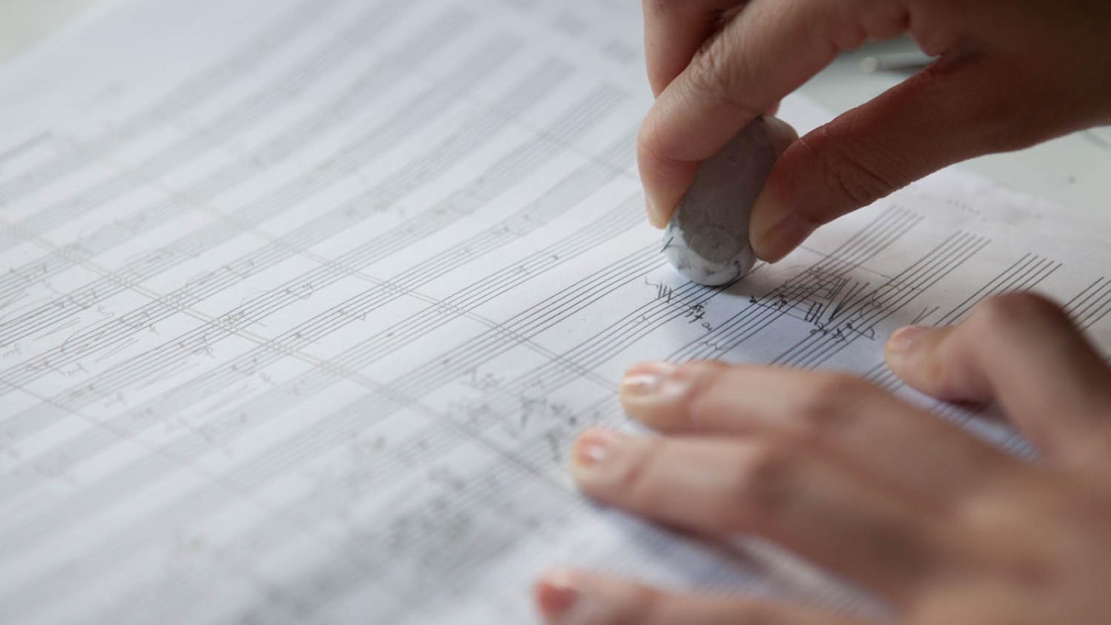 Blick auf eine Kompositionsstudentin, die handschriftliche Eintragungen auf einem Notenblatt ausradiert.