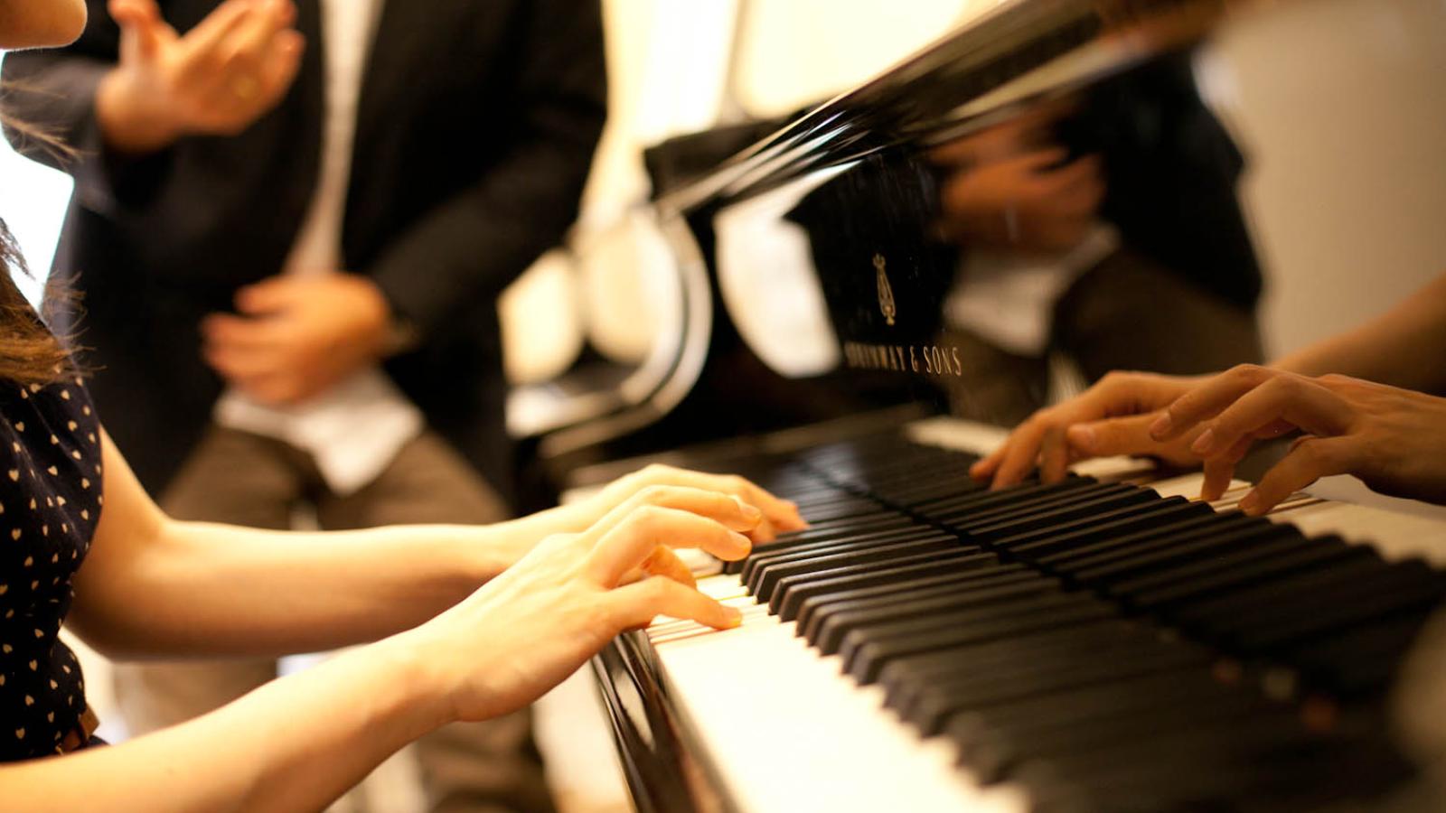 Eine Nahaufnahme einer Pianistin, die am Flügel einen Sänger begleitet.