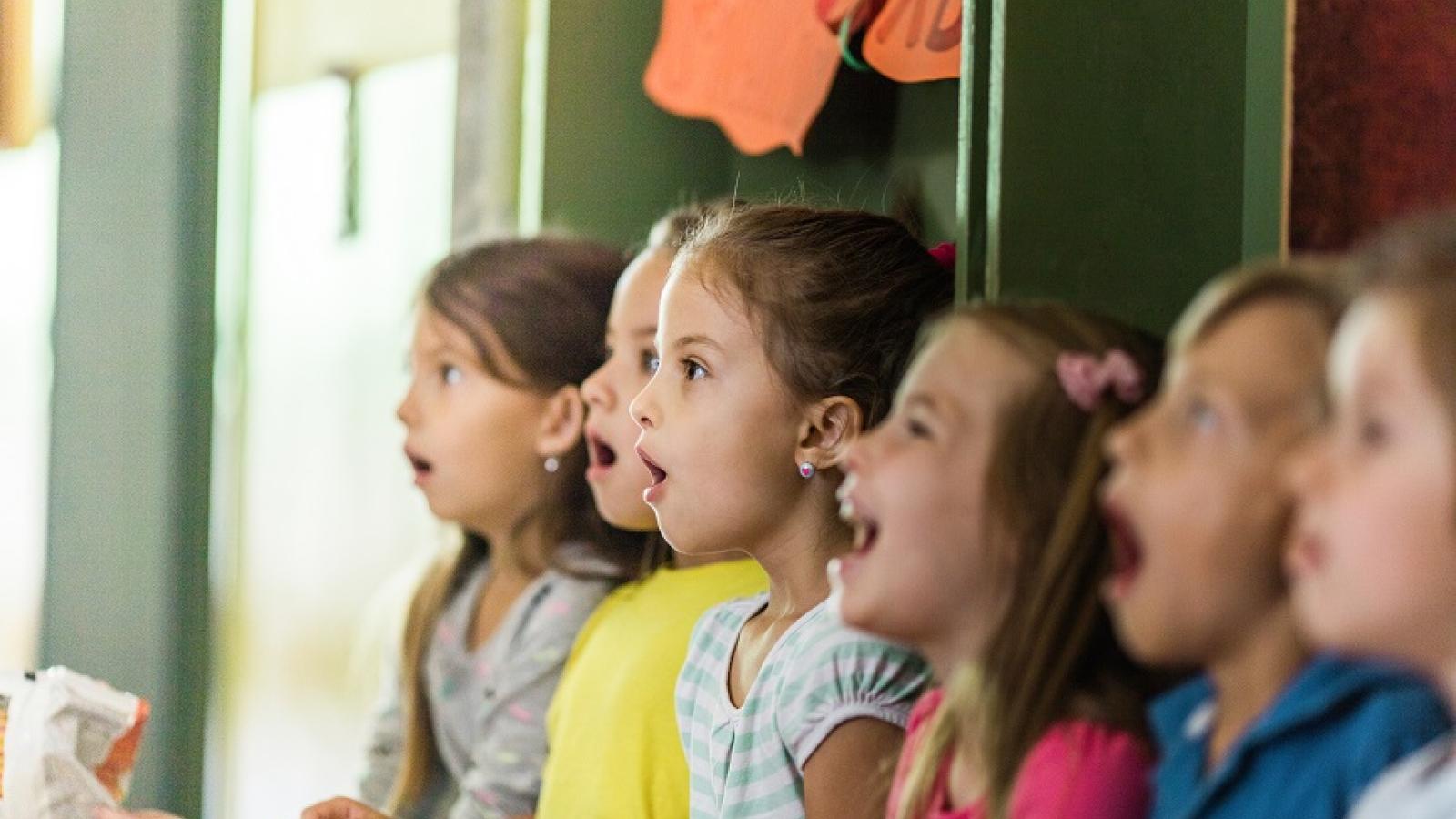 Blick auf eine kleine Gruppe von Kindern im Grundschulalter, die im Musikraum vor einer Tafel singen.