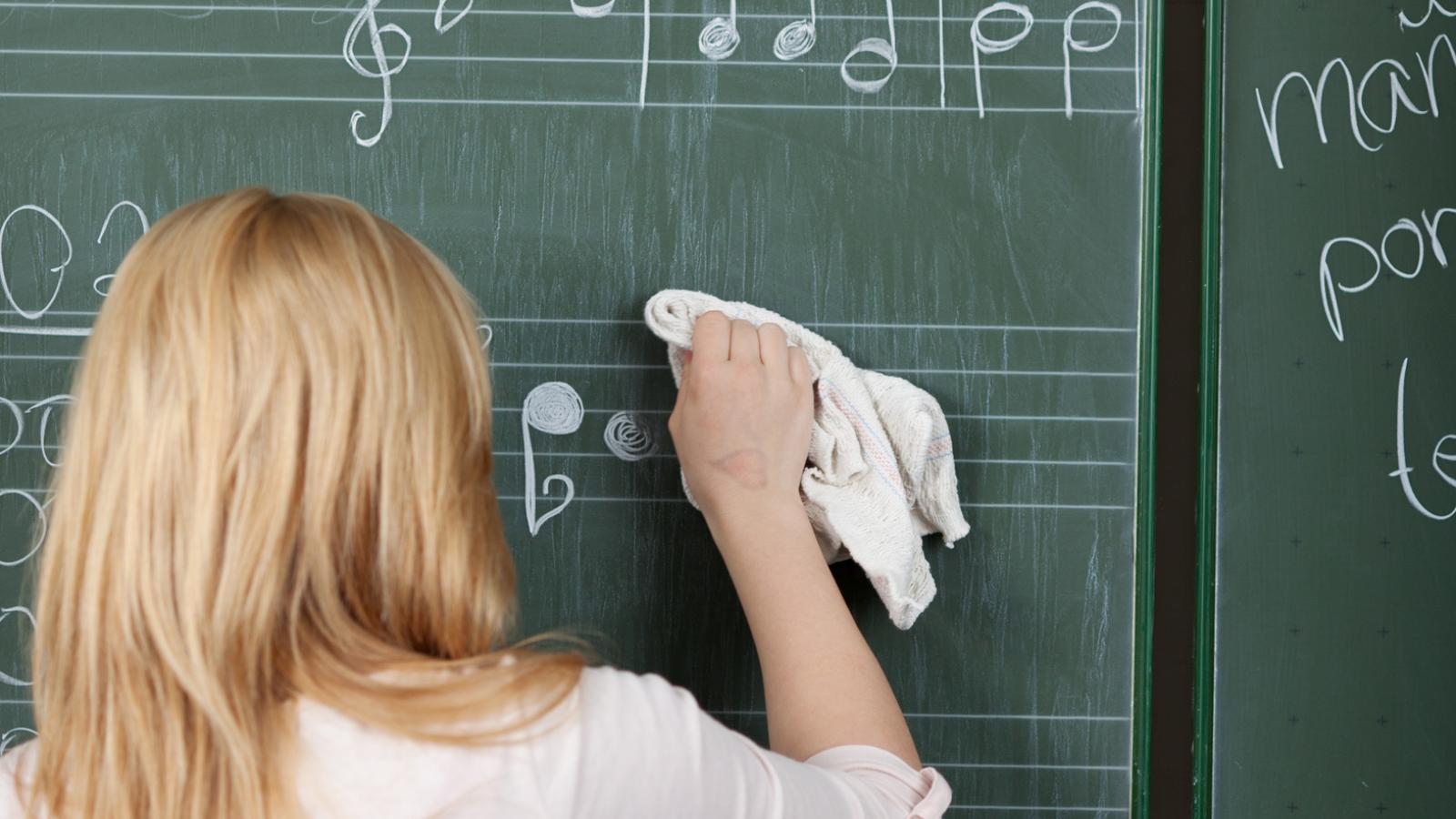 Blick auf eine Schülerin, die von einer Tafel falschen Noten wegwischt