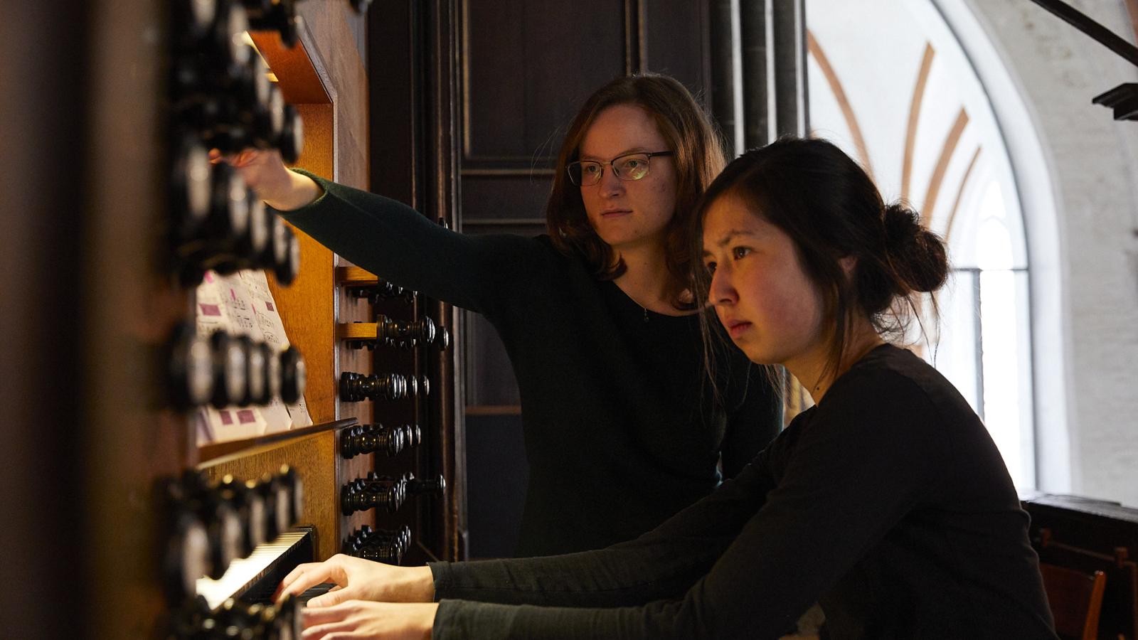 Eine Studentin spielt an der Großen Orgel von St. Jakobi, eine weitere Studentin steht neben ihr und registriert
