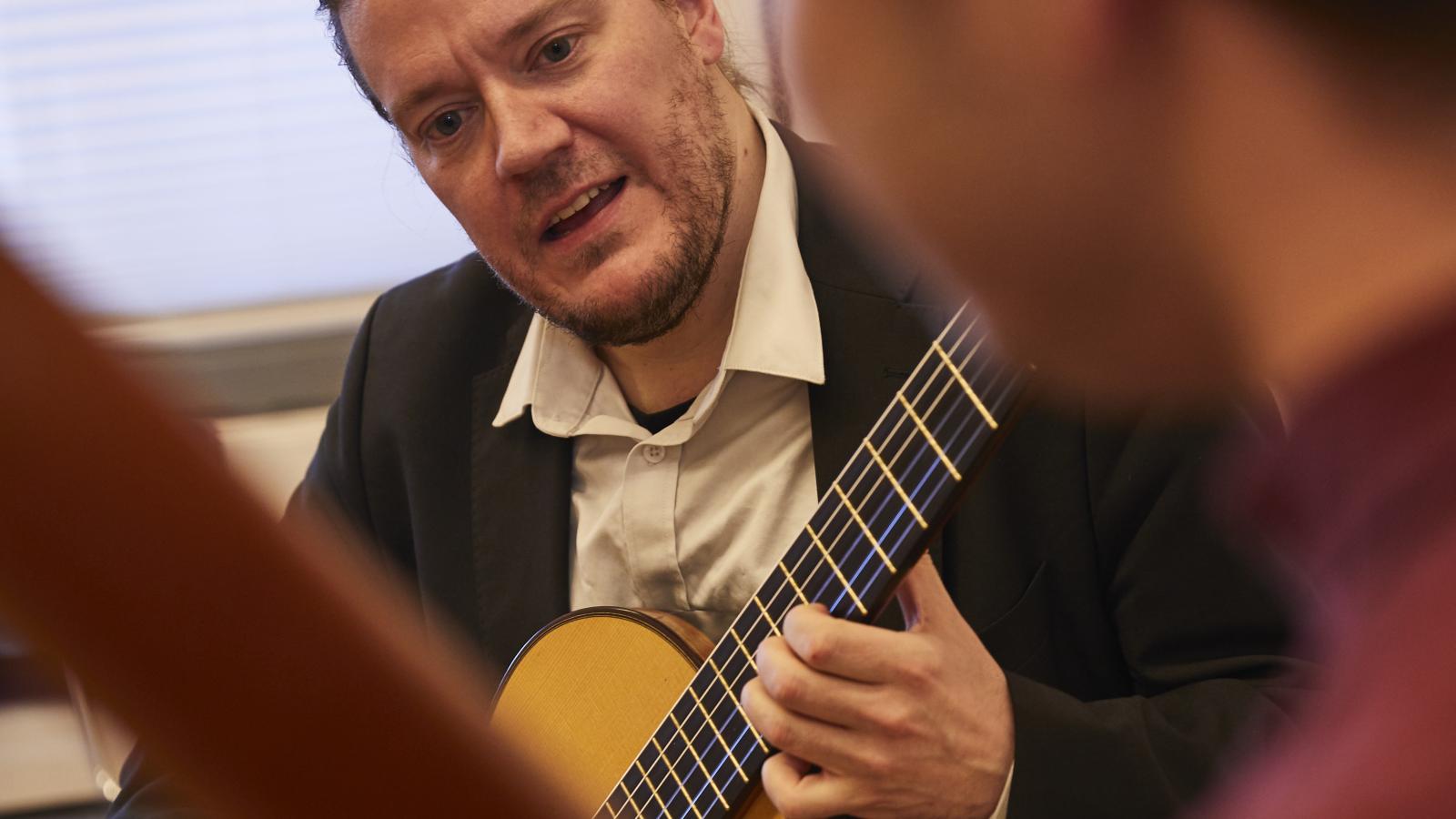Blick in einer Unterrichtssituation zwischen einem Gitarrenlehrer und seinem Studenten