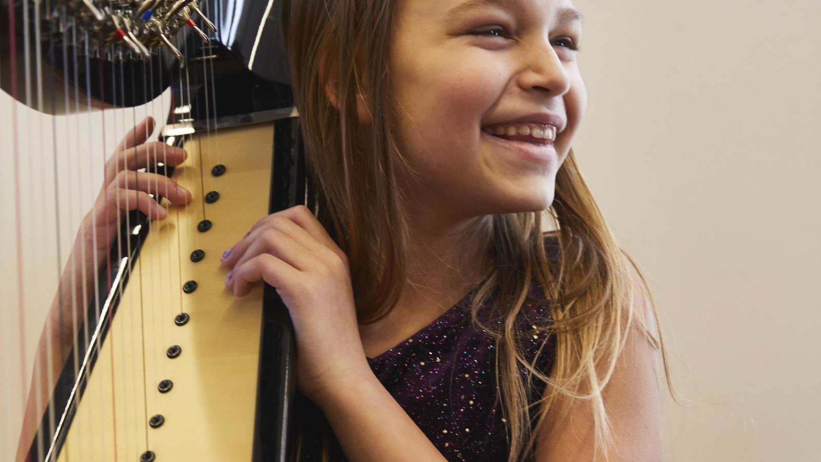 Blick auf eine vor Freude strahlende Harfenschülerin an ihrem Instrument