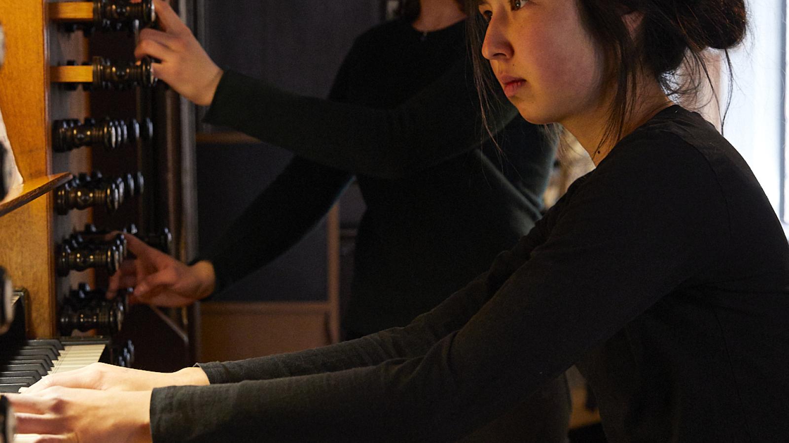 Eine Studentin spielt die Große Orgel in St. Jakobi, eine andere Studentin steht neben ihr und registriert.