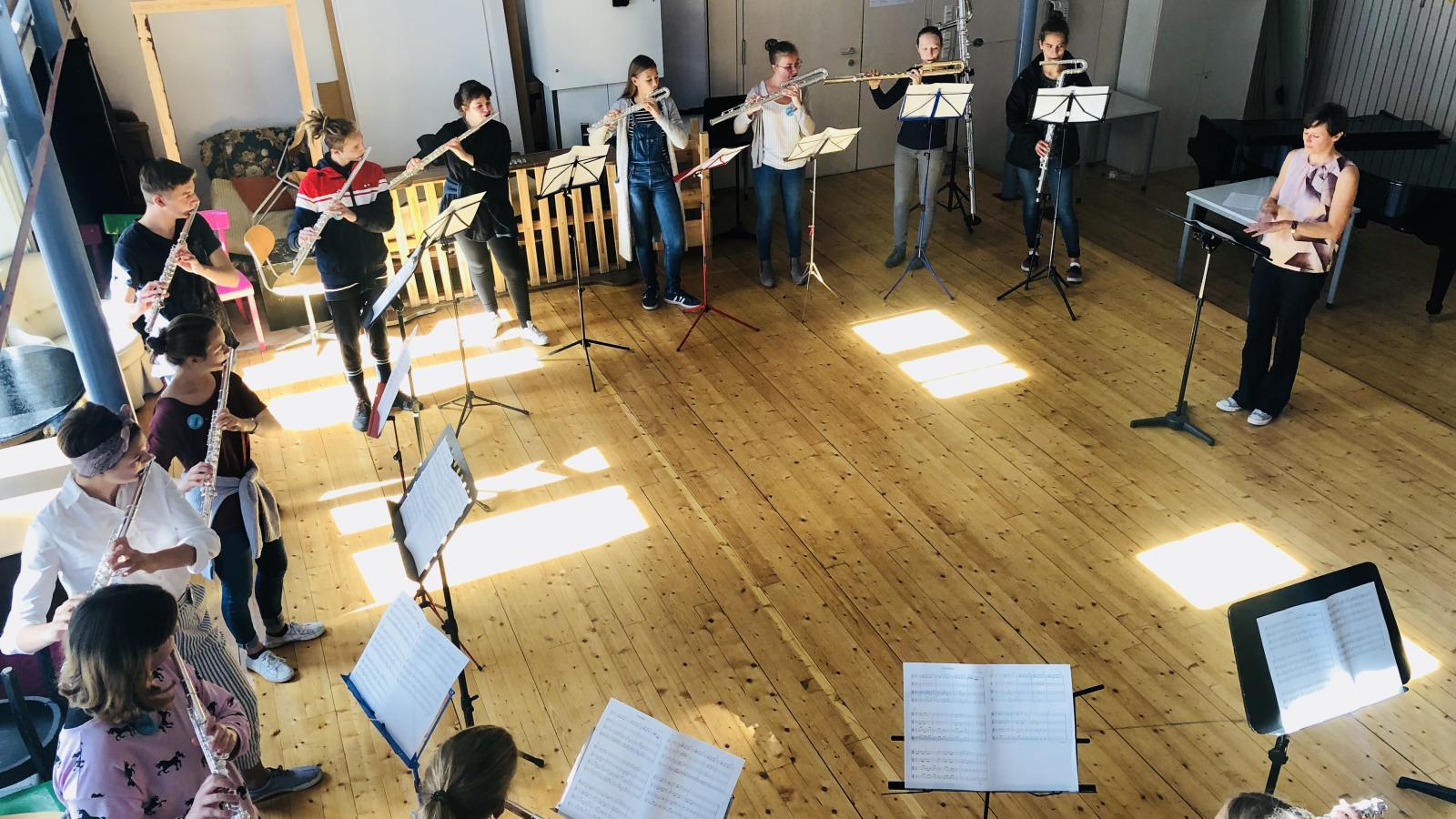 Blick auf eine Gruppe von Querflöte spielenden Schülerinnen und Schülern, die im Kreis stehend mit einander musizieren