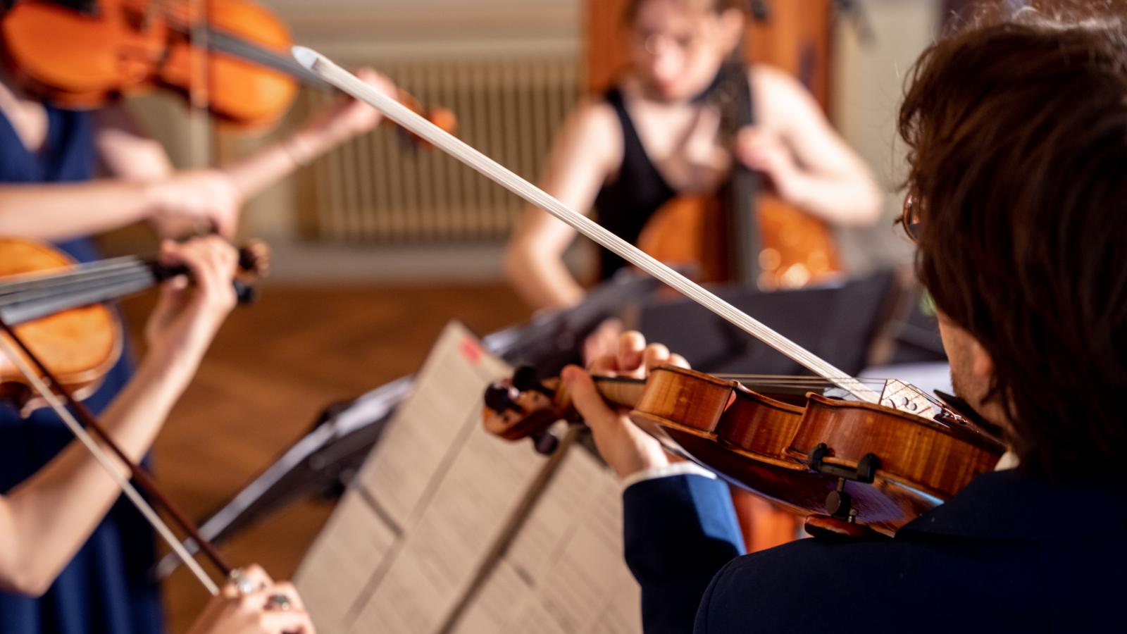 Blick auf vier Studierende, die zusammen ein Sreichquartett spielen