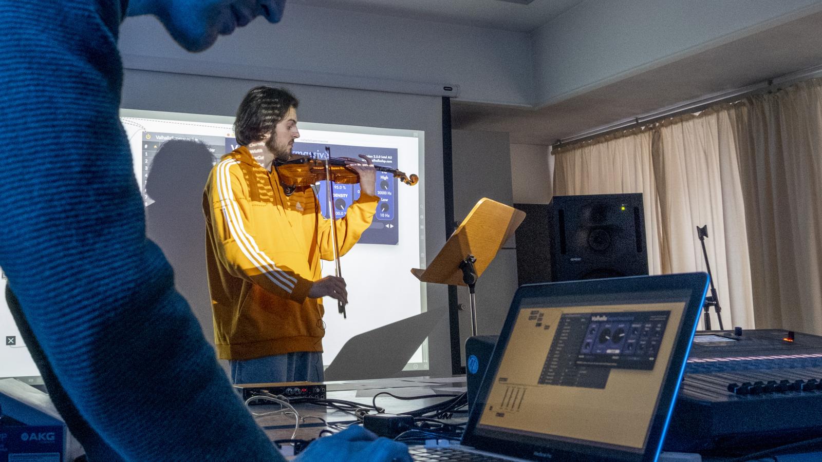 Blick auf zwei Studierende, einer spielt Geige, der andere verfremdete die Klänge mittels eines Computerprogrammse