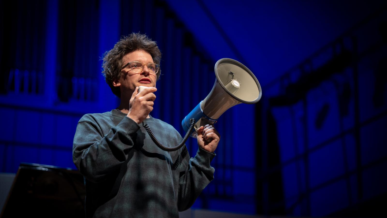 Professor Johannes Fischer mit einem Megaphone auf der Bühne des Großen Saals
