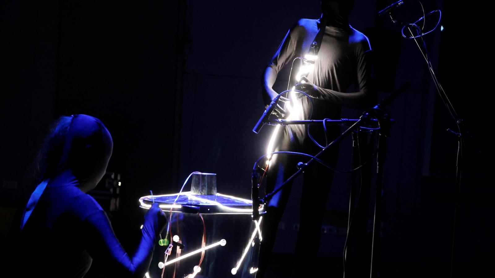 Blick auf zwei komplett in schwarz verhülllte Menschen, die Musik improvisieren