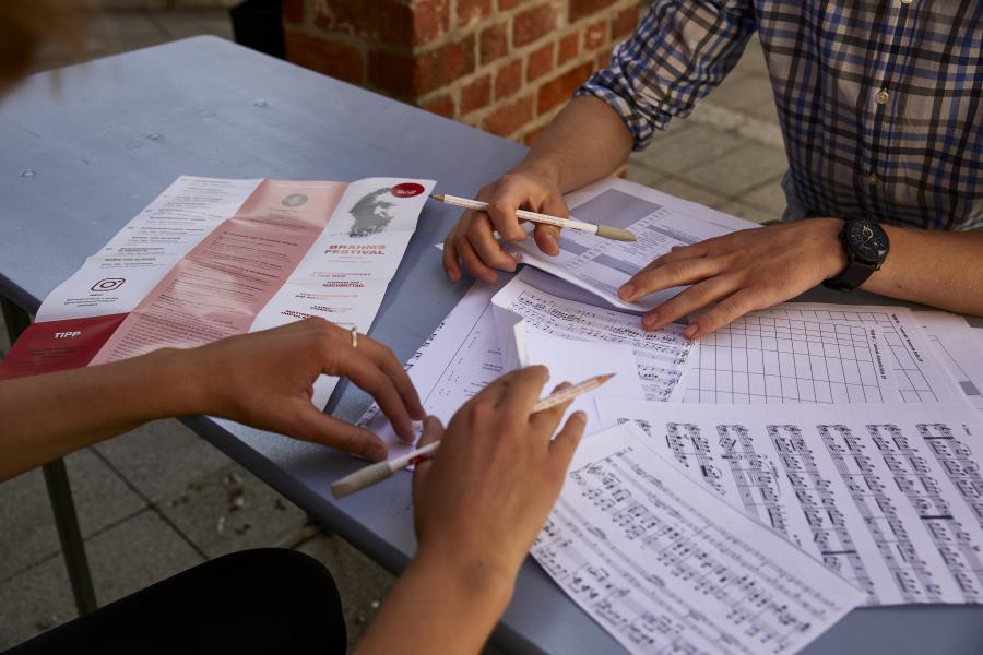 Blick auf vier Hände, die auf einem Tisch unterschiedliche Musiknoten sortieren
