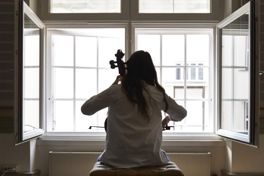 Eine Cellostudentin übt vor einem geöffneten Fenster.