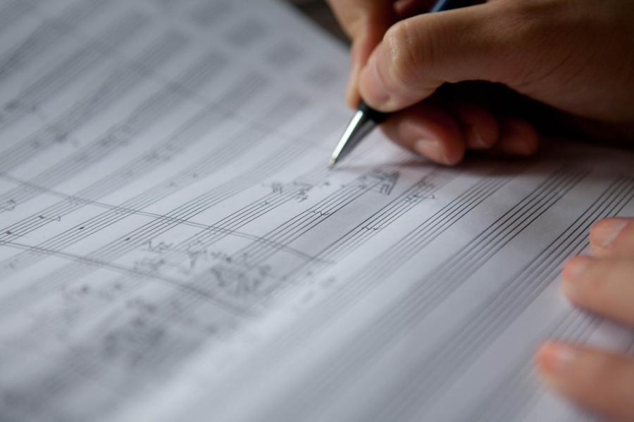 Blick auf eine Hand, die Noten auf Notenpapier schreibt.