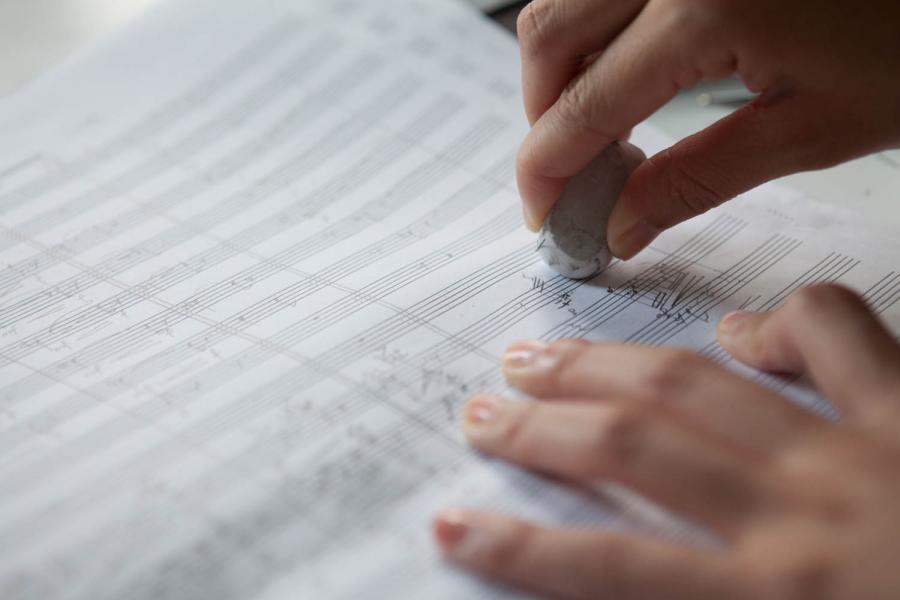 Blick auf eine Kompositionsstudentin, die handschriftliche Eintragungen auf einem Notenblatt ausradiert.