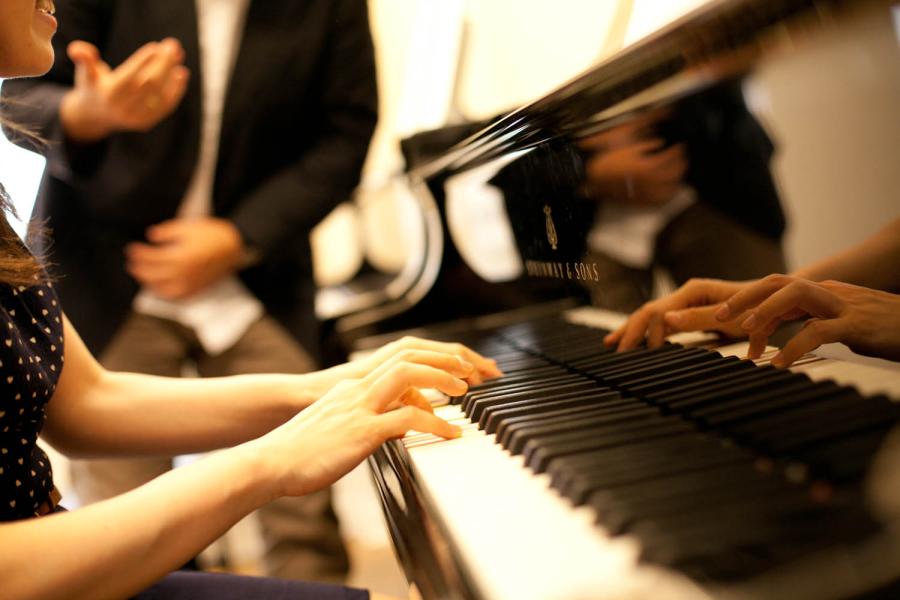 Eine Nahaufnahme einer Pianistin, die am Flügel einen Sänger begleitet.