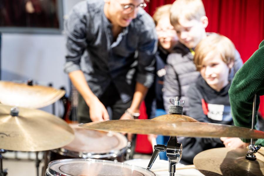 Jugendliche bekommen von einem Studierenden gezeigt, wie man Schlagzeug spielt.