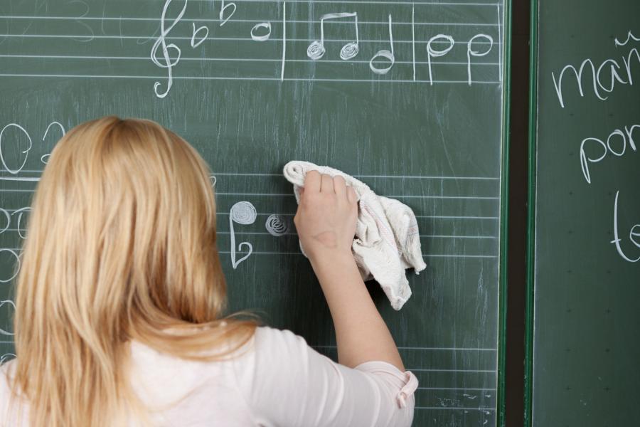 Blick auf eine Schülerin, die von einer Tafel falschen Noten wegwischt