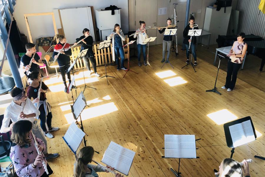 Blick auf eine Gruppe von Querflöte spielenden Schülerinnen und Schülern, die im Kreis stehend mit einander musizieren