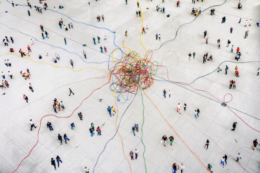Blick auf eine Ansammlung vieler Menschen, die mit bunten Fäden miteinander verbunden sind