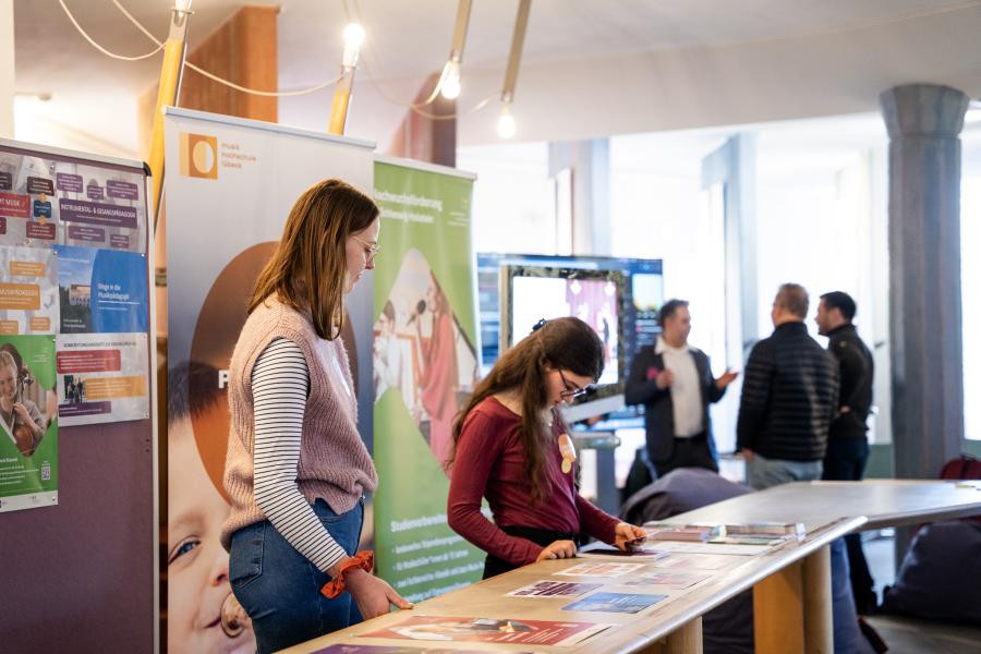 Zwei Studentinnen stehen an einem Informationsstand zu den MHL-Studiengängen.