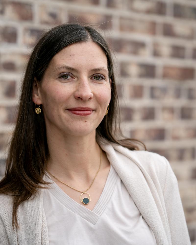 Prof. Anna-Unger Rudroff ist vor einer roten Backsteinwand zu sehen und schaut lächelnd in die Kamera