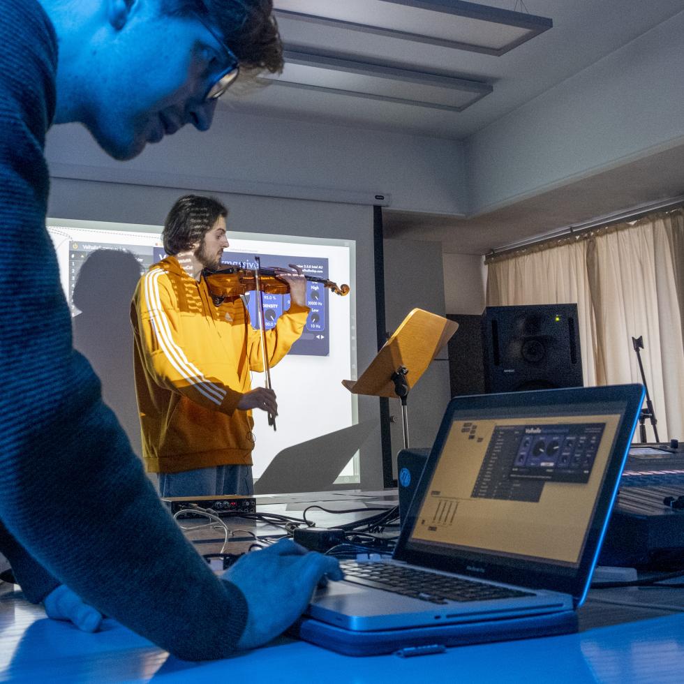 Blick auf zwei Studierende, einer spielt Geige, der andere verfremdete die Klänge mittels eines Computerprogrammse