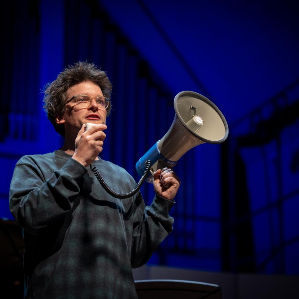 Professor Johannes Fischer mit einem Megaphone auf der Bühne des Großen Saals