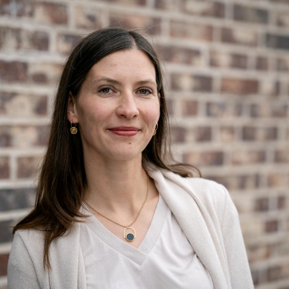 Prof. Anna-Unger Rudroff ist vor einer roten Backsteinwand zu sehen und schaut lächelnd in die Kamera