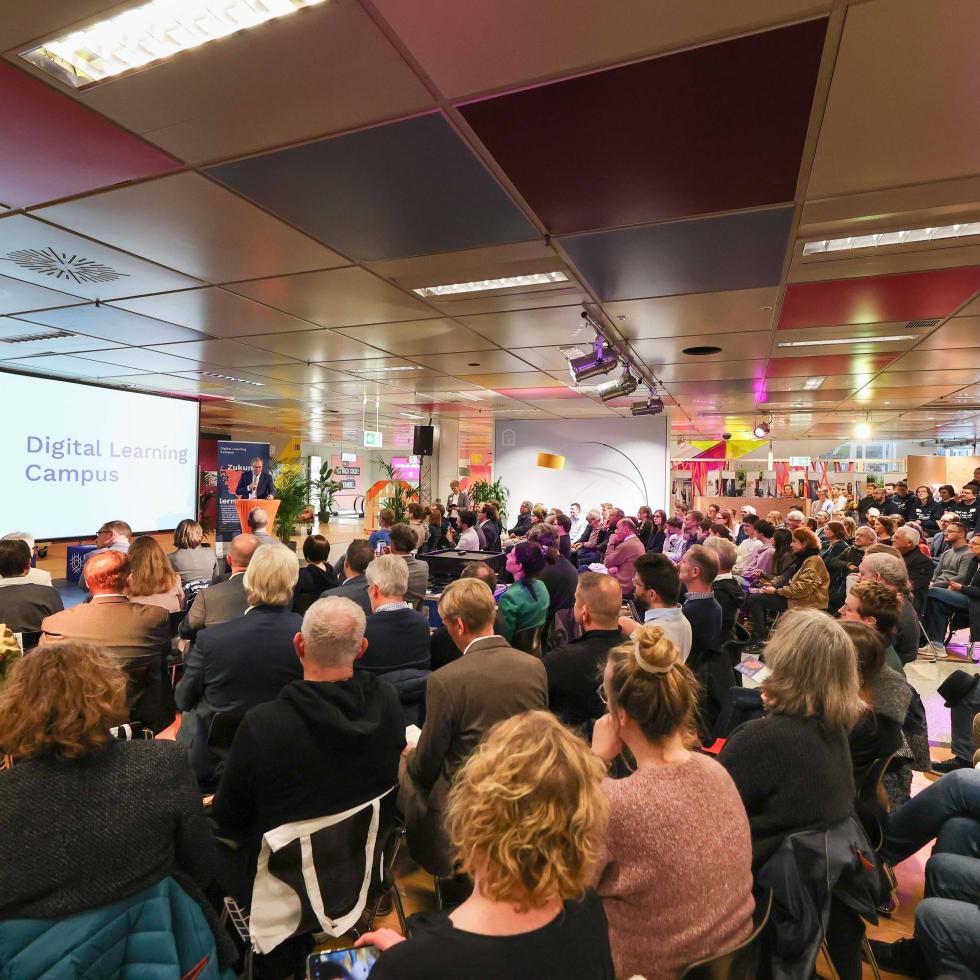 Vortrag im Übergangshaus, Menschen schauen zur leinwand wo, digital learning campus steht, 