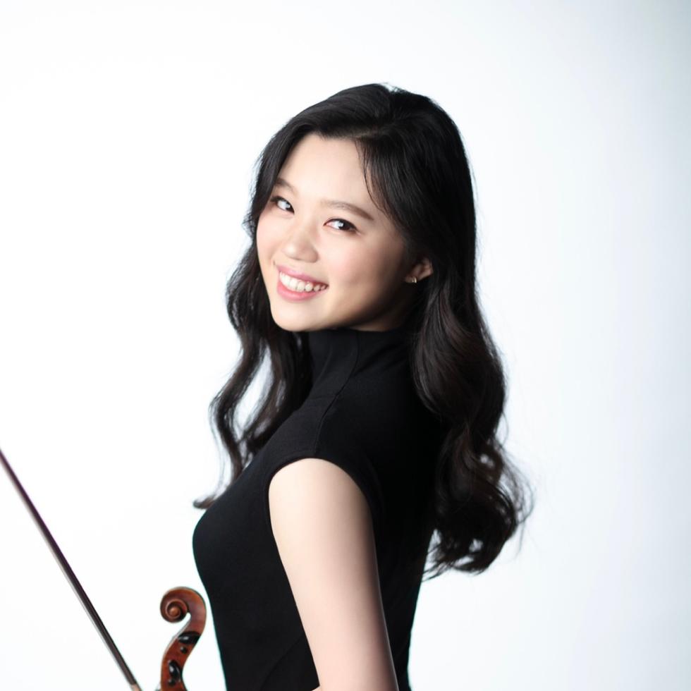 Hyunseo Cho lächelnd zur Kamera, körper zur Seite gedreht mit Violine und Bogen in den Händen 