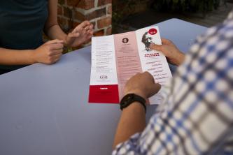 Zwei Studierende schauen sich im Mensahof das MHL-Monatsprogramm an, um sich über aktuelle Veranstaltungen zu informieren.